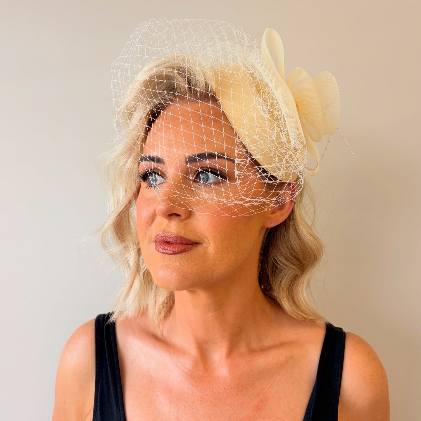 Soft blonde waves finished with a cream fascinator and birdcage veil