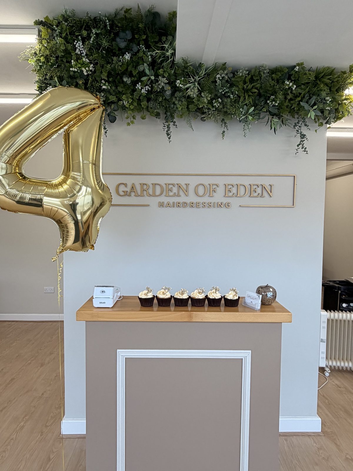Reception desk beneath the Garden of Eden hairdressing sign and a foliage garland