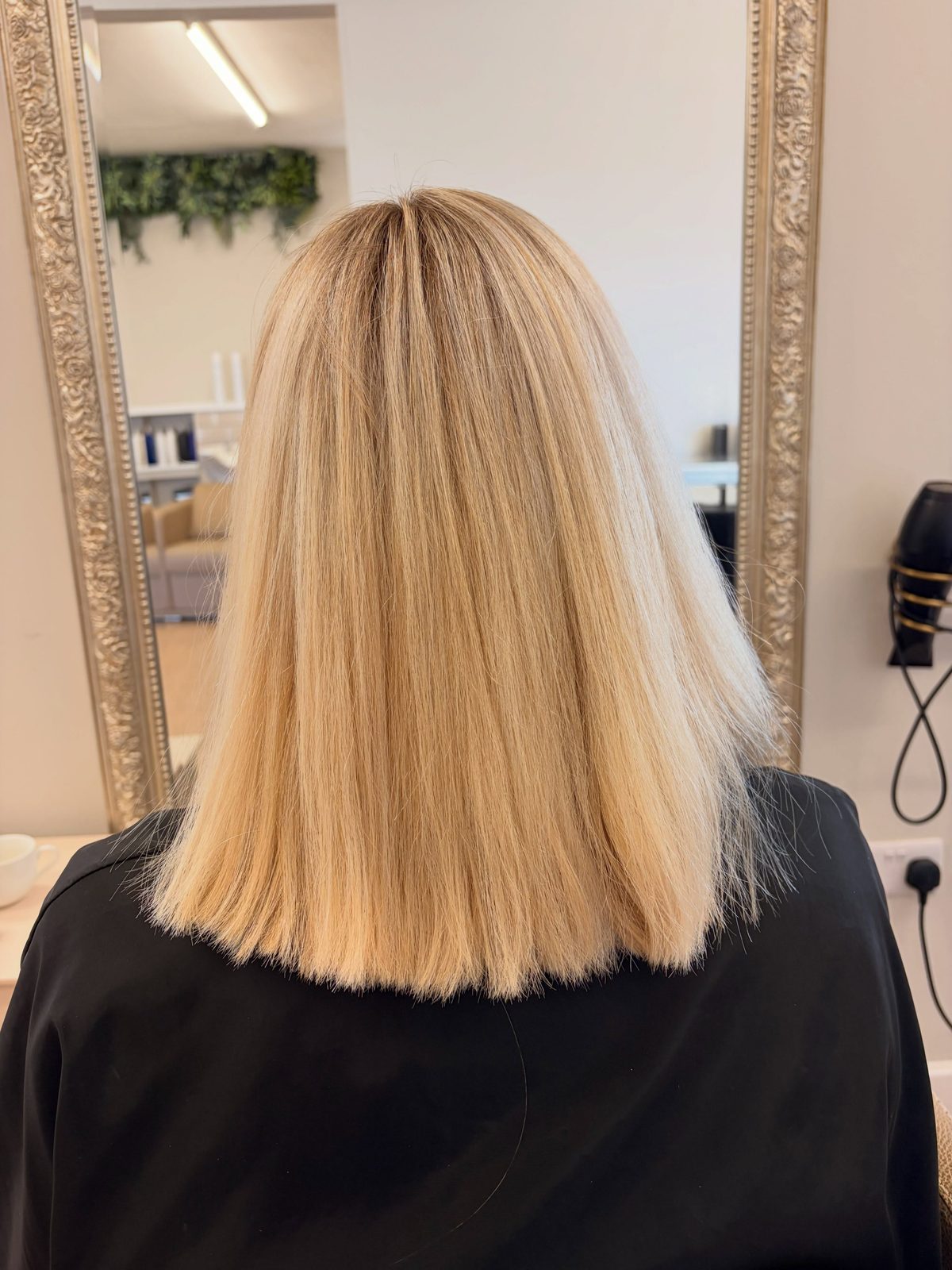 Sleek blonde blunt cut, back view in front of the salon mirror